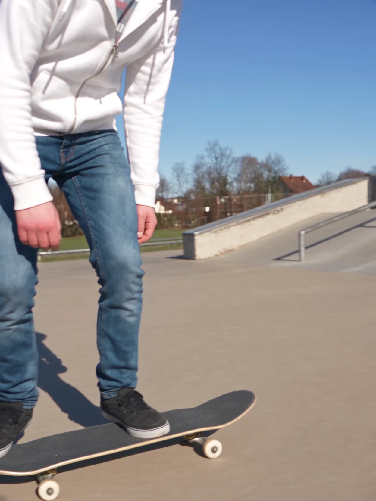 Start frame: Jeff standing on his board on the flat concrete of a skatepark, framed from the chest down
